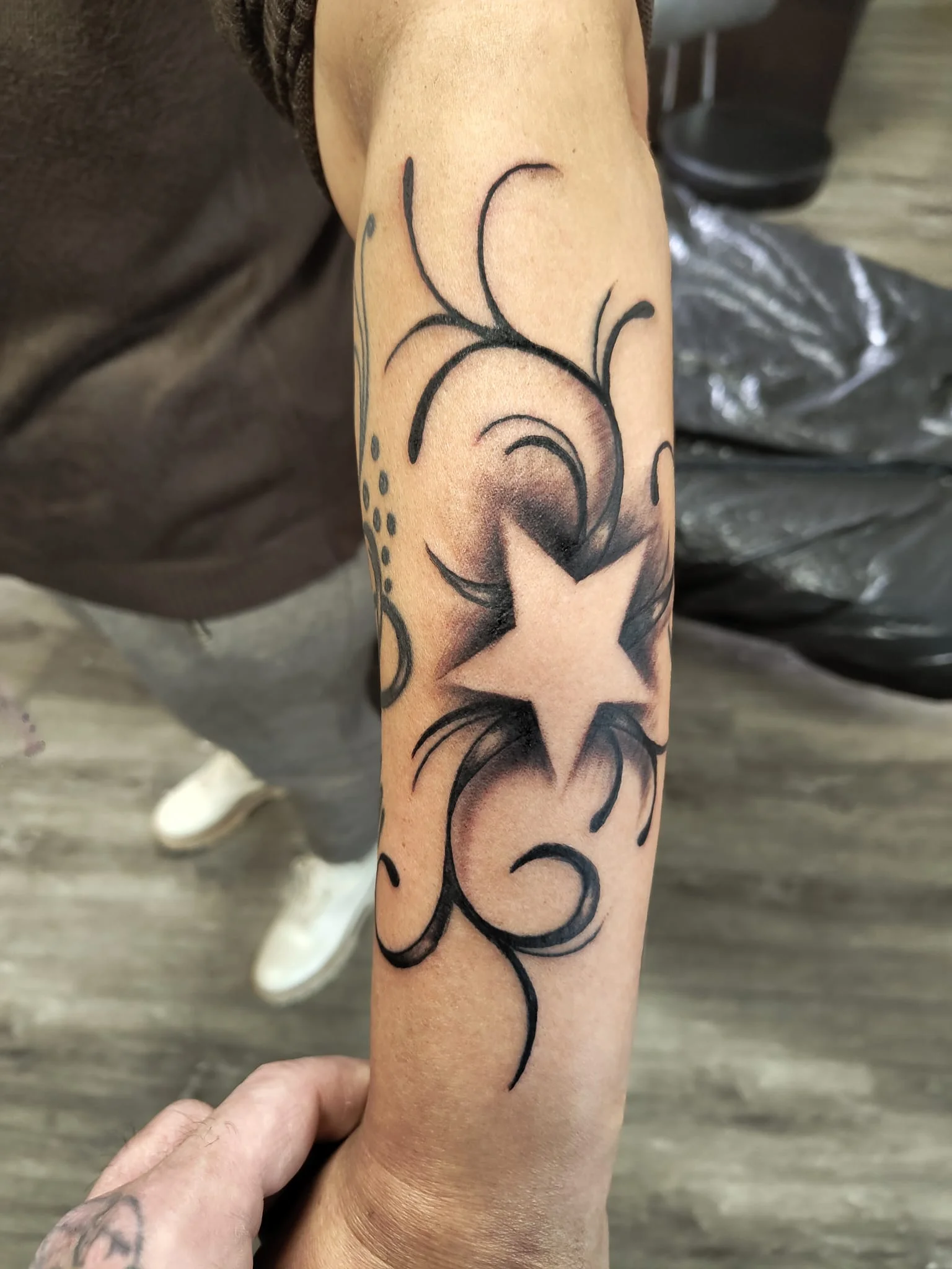 Black and Grey Stern-Tattoo mit schwungvollen Schnörkeln, gestochen von Lutz im Living Pictures Studio.